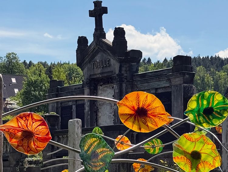 Bunte Glasblätter vor einem alten, großen Grabstein
