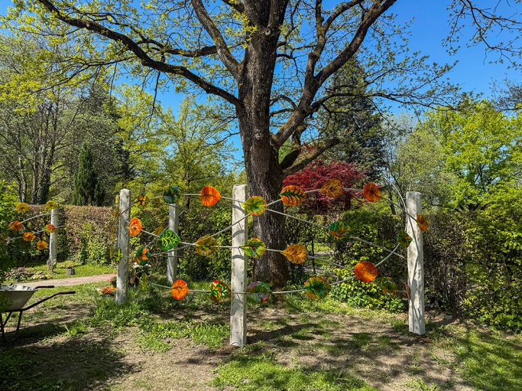 45 bunte Glasblätter strahlen vor einer Hecke. 45 bunte Glasblätter strahlen vor einer Hecke.