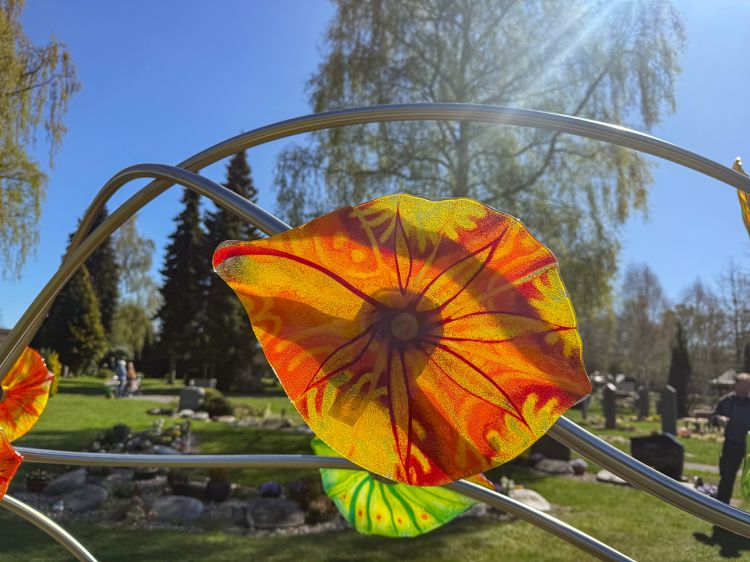Ein Gelb-Oranges Glasblatt was von der Sonne angestrahlt wird. Das Blatt ist von Edelstahlrohren umschlungen. Ein Gelb-Oranges Glasblatt was von der Sonne angestrahlt wird. Das Blatt ist von Edelstahlrohren umschlungen.