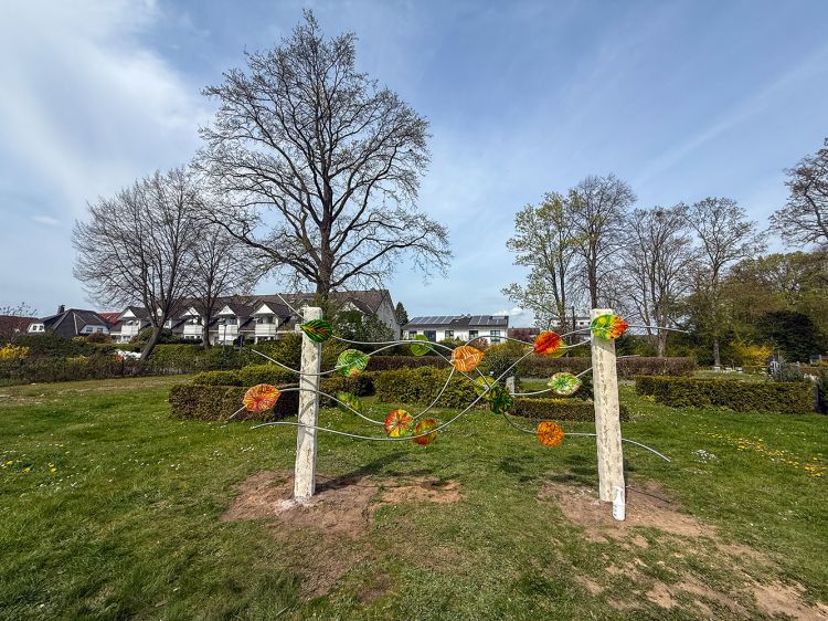 Urnen-Gemeinschafts-Grabanlage mit 16 bunten Glasblättern, Blauer Himmel und Bäume im Hintergrund. Urnen-Gemeinschafts-Grabanlage mit 16 bunten Glasblättern, Blauer Himmel und Bäume im Hintergrund.