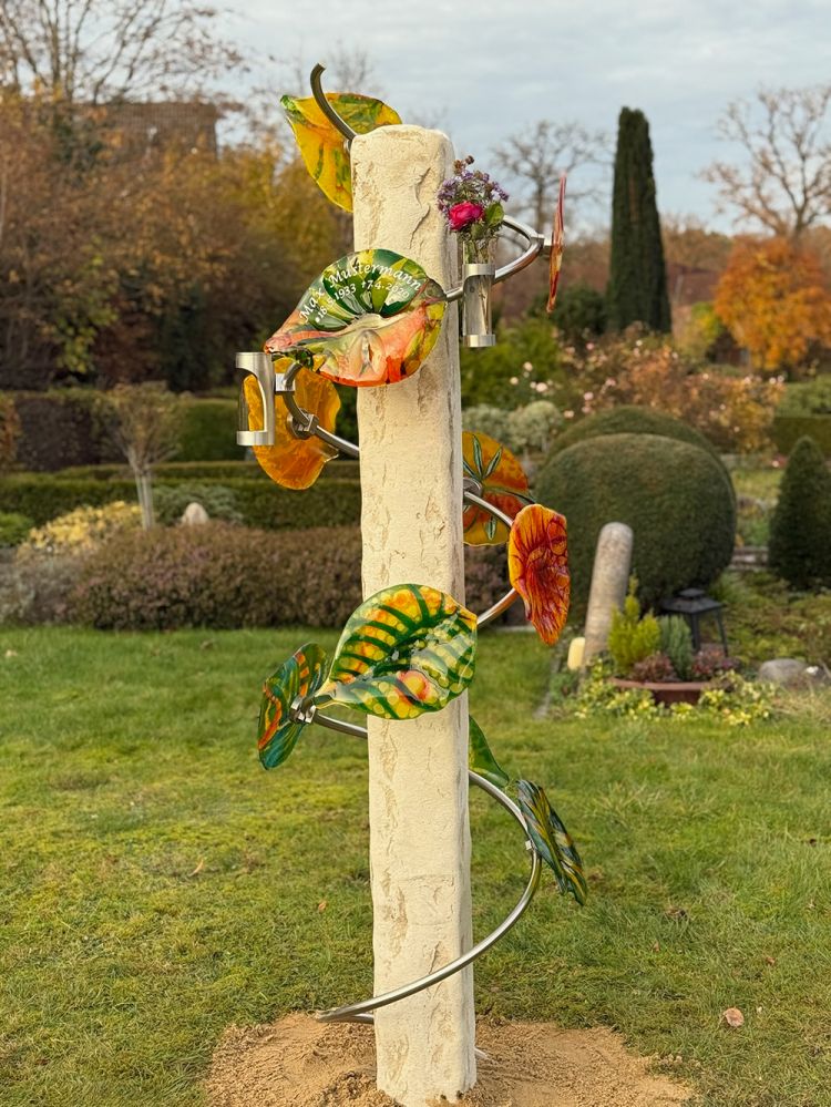 Steinerne Urnengemeinschaftsgrab-Säule mit Metallvase und bunten Glasblättern auf dem Friedhof